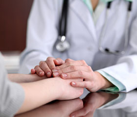 Médico sosteniendo las manos de un paciente, mostrando apoyo y compasión