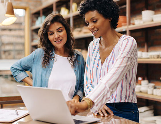 Dos mujeres trabajadoras en un local de cerámica señalando un detalle en el portátil