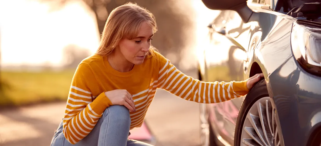 Persona preocupada mirando el neumático de un coche